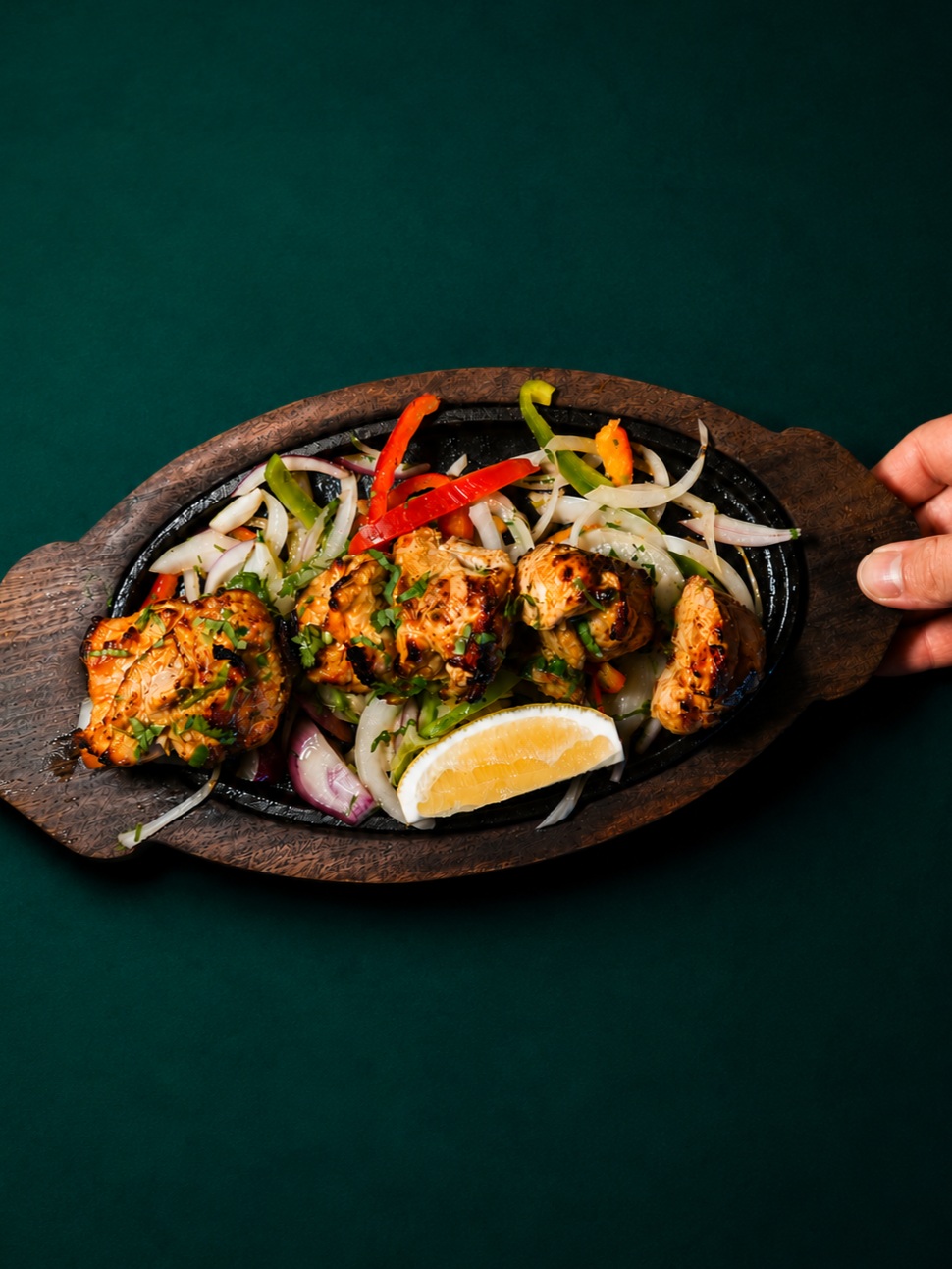Char-grilled chicken tikka with peppers, onions and a lemon wedge on a sizzler plate